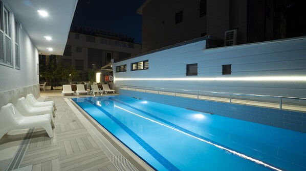 An outdoor swimming pool with lounge chairs and a tiled deck.