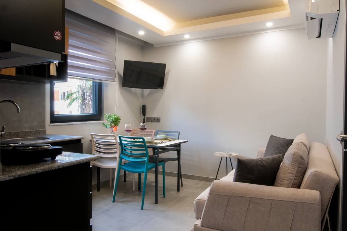 Una cocina compacta con comedor, un sofá y un televisor instalado en la pared.
