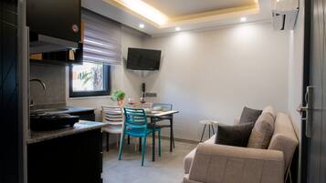 Una cocina compacta con comedor, un sofá y un televisor instalado en la pared.