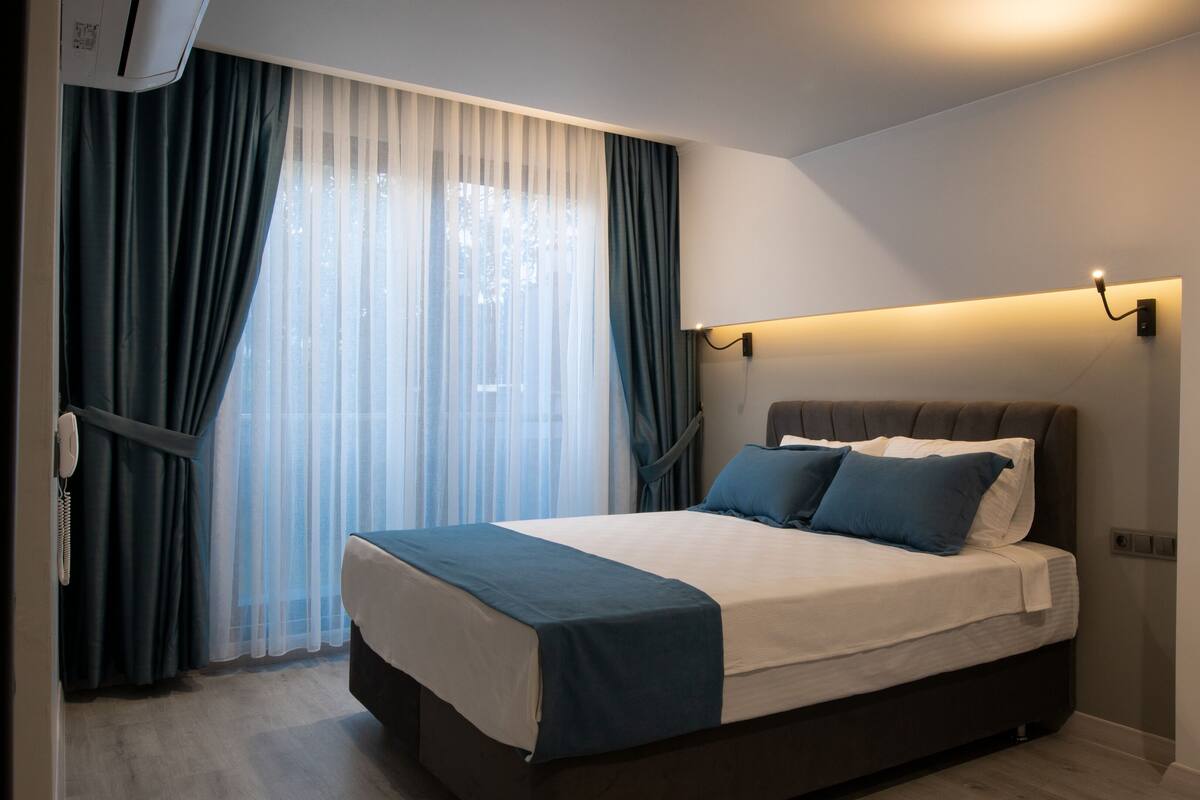 Una habitación de hotel moderna con una cama grande, cortinas oscuras y una lámpara fijada a la pared.
