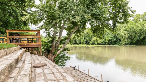 Eine Holzterrasse führt zu einem Steg über einem ruhigen See, umgeben von üppigem Grün.