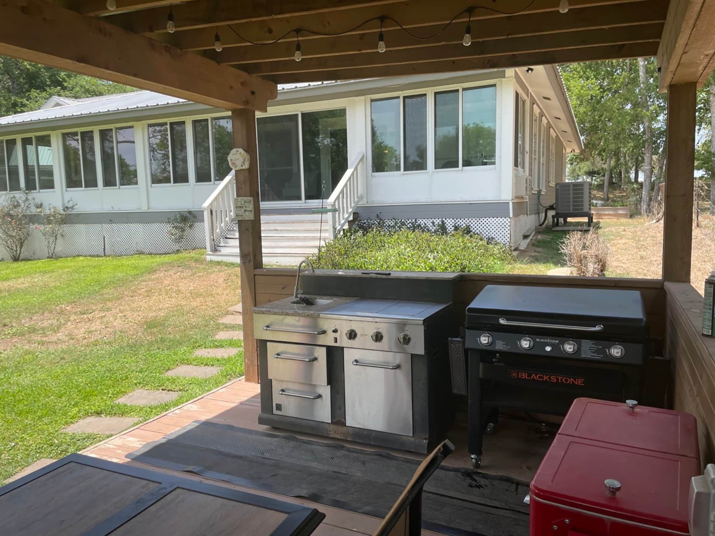 An outdoor kitchen area with a grill and a sink, under a wooden pergola with string lights.