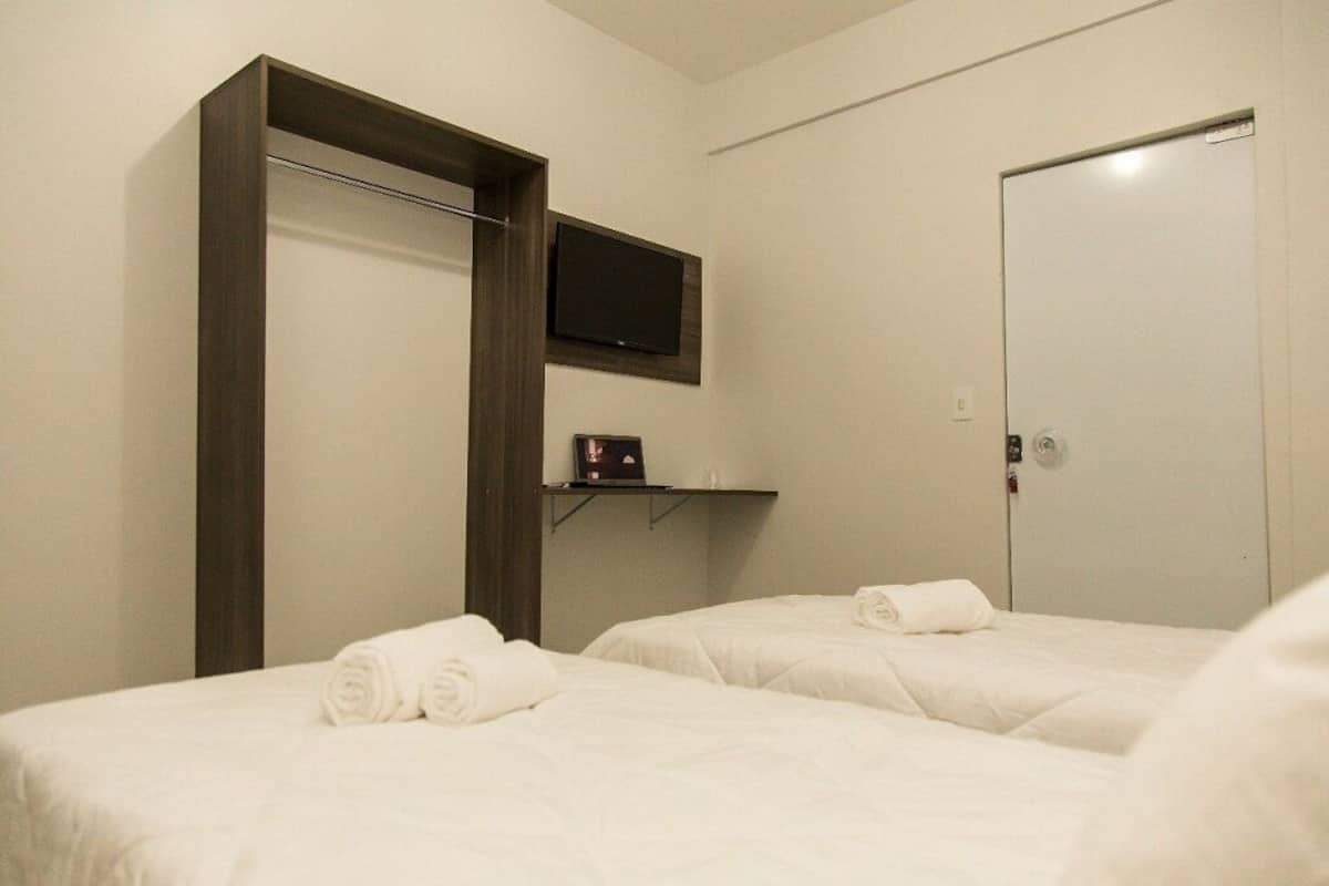 Ein Hotelzimmer mit zwei Betten, einem an der Wand befestigten Fernseher und einer Tür.