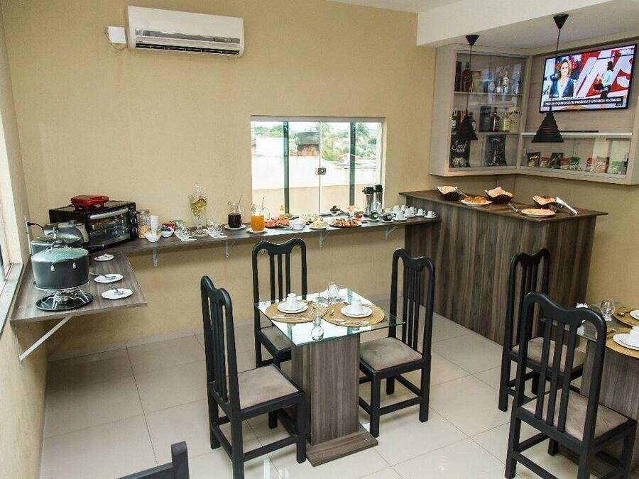 Un restaurante con una mesa de vidrio, sillas, un televisor y una zona de bar con botellas y vasos.
