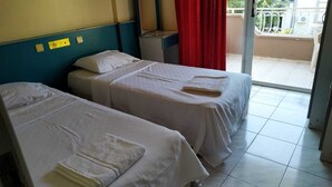 Due letti singoli con lenzuola e asciugamani bianchi, una piccola scrivania, una tenda rossa e un balcone con ringhiera bianca.