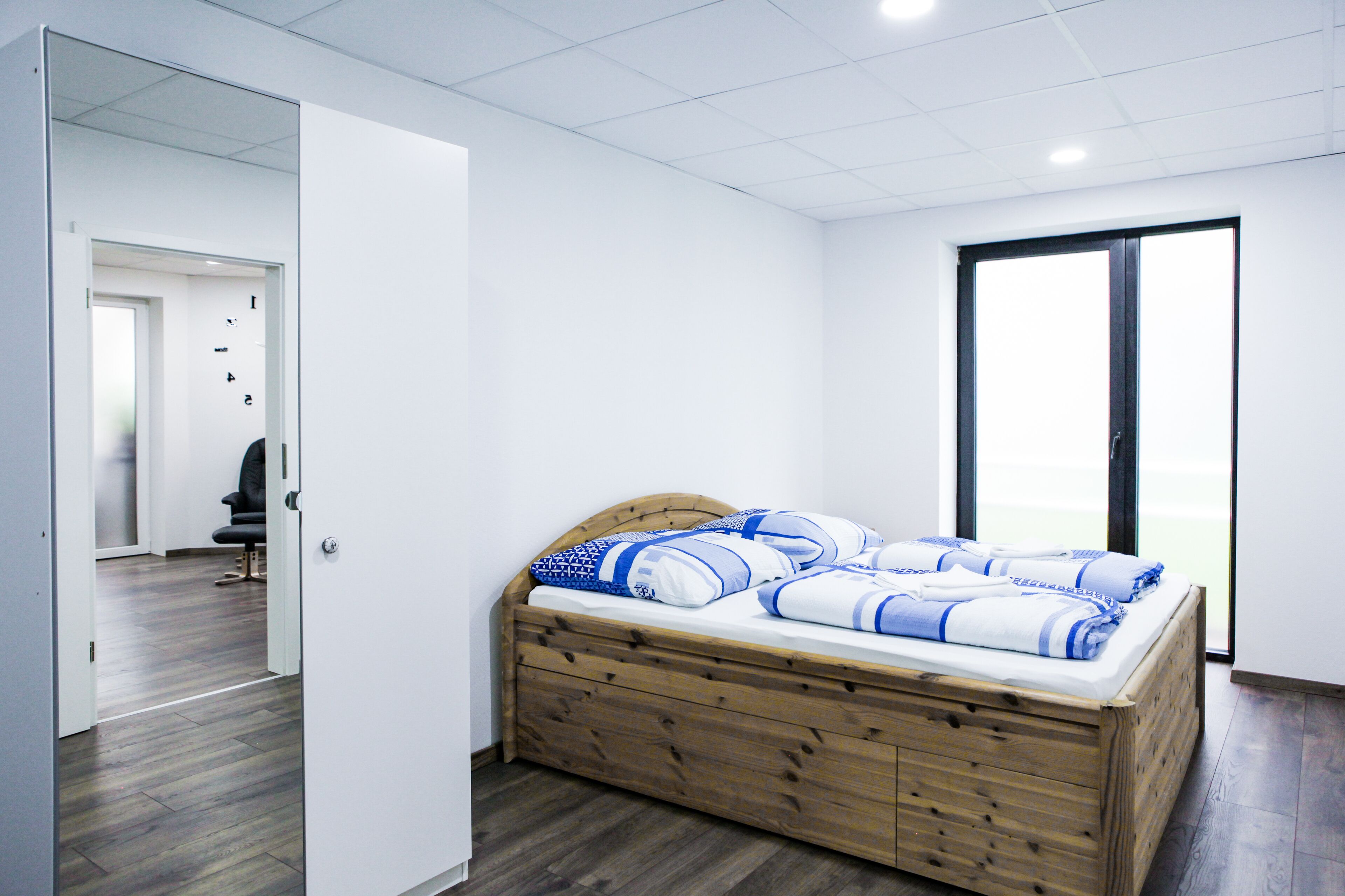 A bedroom with a wooden bed, white walls, and a large window.