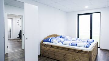 A bedroom with a wooden bed, white walls, and a large window.