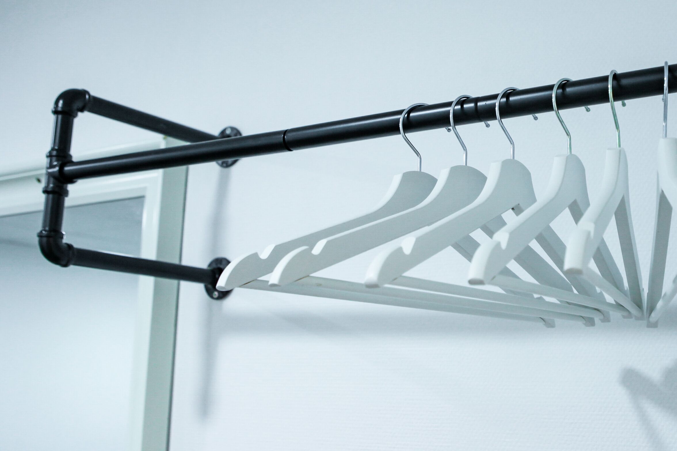 A black metal drying rack with white hangers against a white wall.