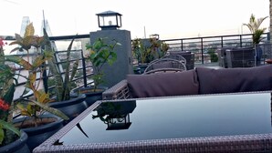 A rooftop terrace with wicker furniture, potted plants, and a view of the cityscape. - Meridian C.A (Dar es Salaam)