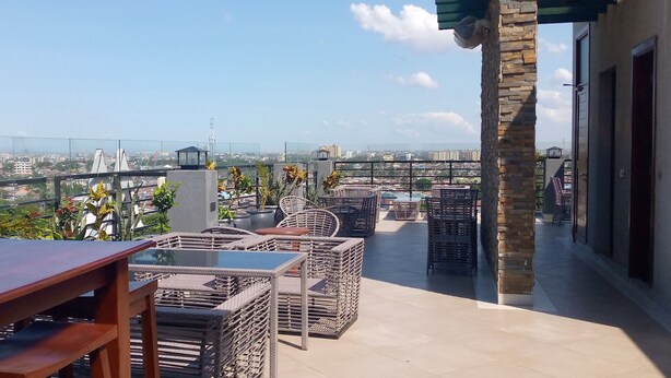 A rooftop terrace with wicker furniture, a glass table, and a view of the cityscape. - Meridian C.A (Dar es Salaam)