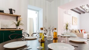 Et spisebord dækket med tallerkener, bestik og glas, med et køkken i baggrunden.
