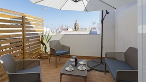 A terrace with wicker furniture, a table with cups and a kettle, and a large umbrella.