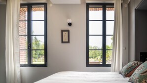 Ein Schlafzimmer mit einem großen Bett, zwei Vorhängen und einem Fensterblick sowie einem gerahmten Bild an der Wand.