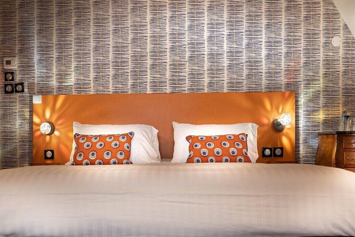 A hotel room with a large bed, patterned wallpaper, and a wooden headboard.