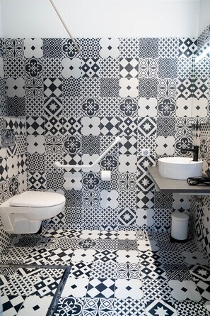 Un baño con pared de azulejos estampados, inodoro, lavamanos y zona de ducha.