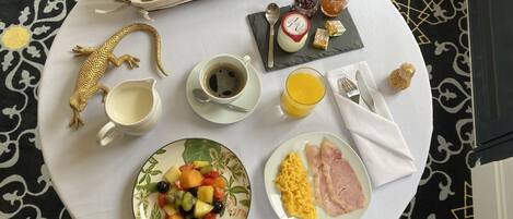 Een ontbijt met croissants, fruit, roerei, ham, koffie en sap op een tafel.