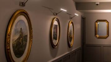 A hallway with framed artwork on the wall, recessed lighting, and a security camera.