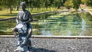 Eine Statue, die eine Person zeigt, wie sie eine Scheibe hält, sitzend auf einem Felsen an einem Teich mit Seerosen.