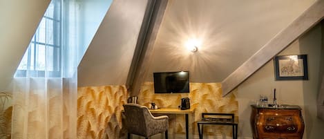 Une chambre confortable située sous les toits, avec un plafond en pente, un bureau avec une chaise, une télévision et une petite commode en bois.