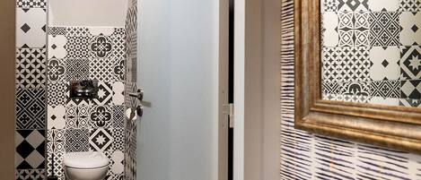 Un pasillo estrecho con baldosas blancas y negras formando un diseño, que lleva a un baño con inodoro y espejo.