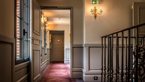Ein Flur mit einem gemusterten Teppich, einer Treppe mit aufwendiger Balustrade und einer Wandleuchte.