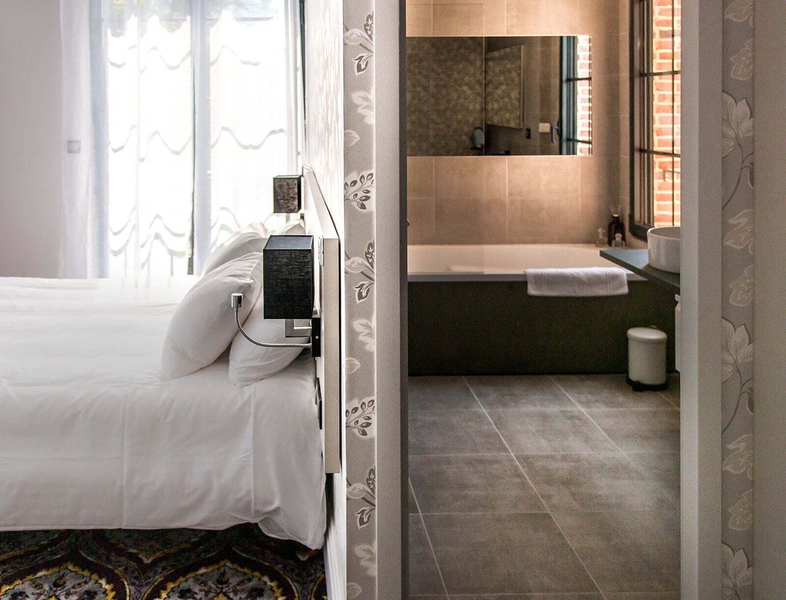 Una habitación de hotel con cama, baño con bañera y un cubo de basura a la vista.