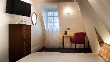 Un dormitorio con cama, cómoda, escritorio con silla, televisor montado en la pared y ventana con cortina.