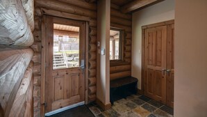 A log cabin interior with a wooden door, a bench, and a stone-tiled floor.