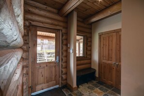 A log cabin interior with a wooden door, a bench, and a stone-tiled floor.