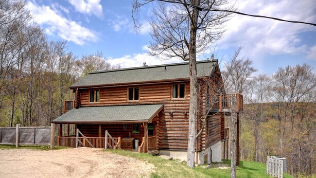 A two-story log cabin with a front porch and a fenced yard.