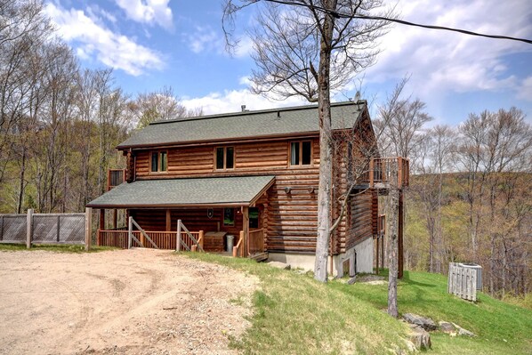 A two-story log cabin with a front porch and a fenced yard.