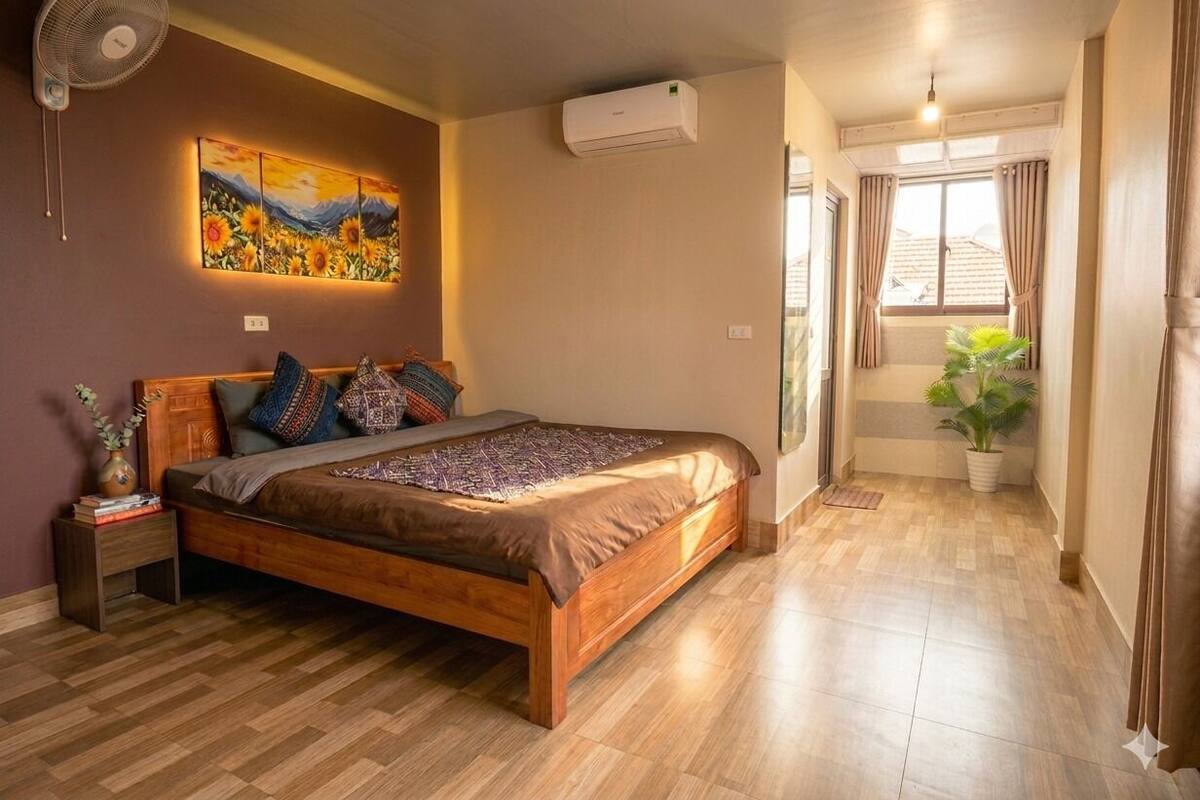 A bedroom with a wooden bed, a wall-mounted air conditioner, a ceiling fan, and a painting.