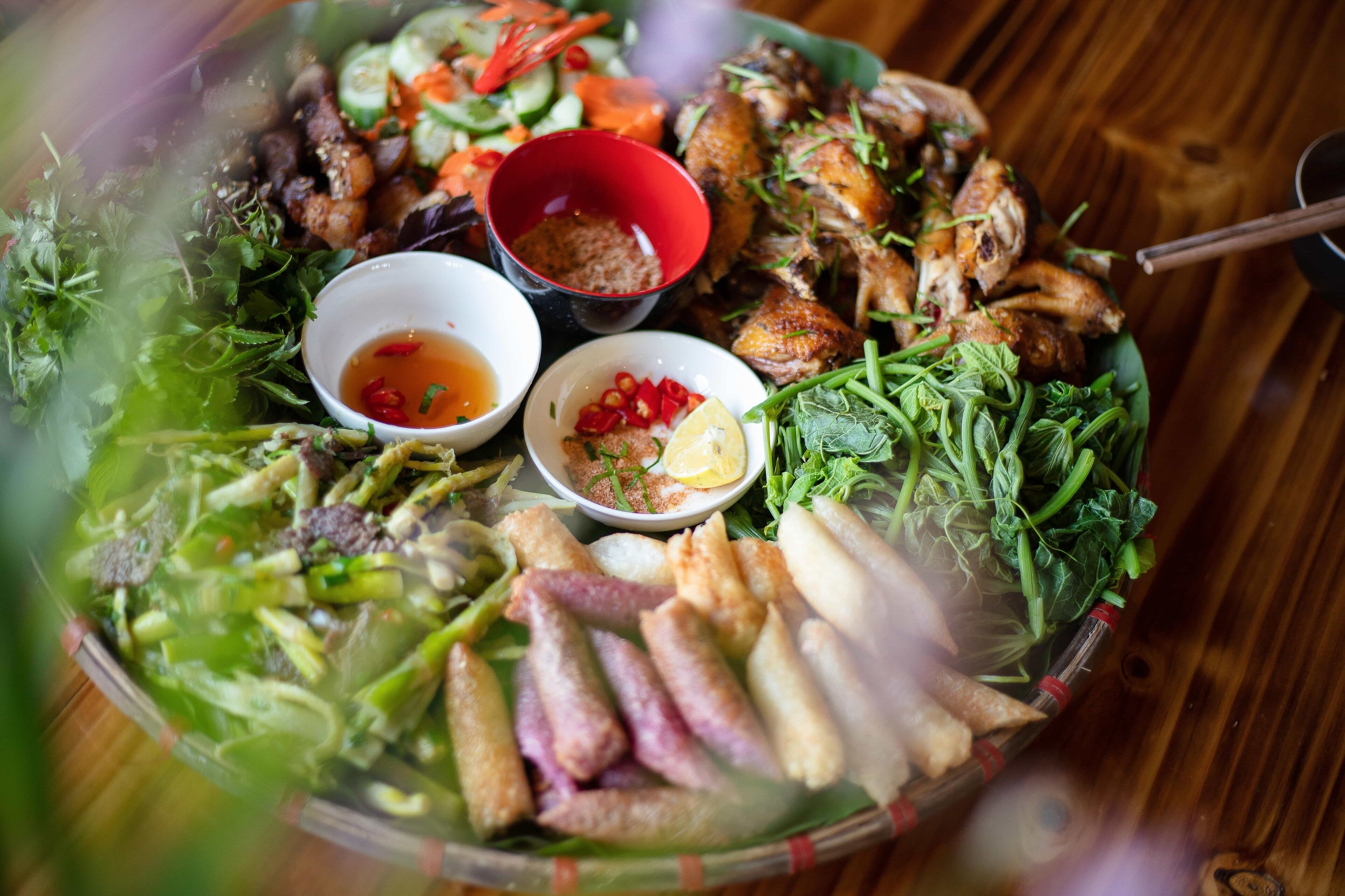 A variety of dishes including grilled meats, vegetables, and dipping sauces on a wooden table.