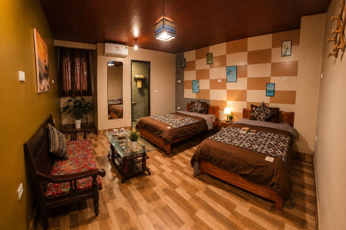 A hotel room with two beds, a wooden floor, a dining table, a sofa, and a mirror.