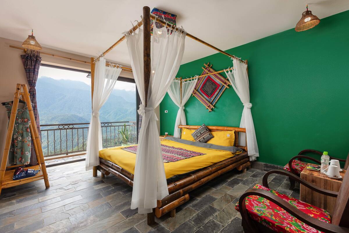 A room with a bed, a chair, a table, and a view of mountains.