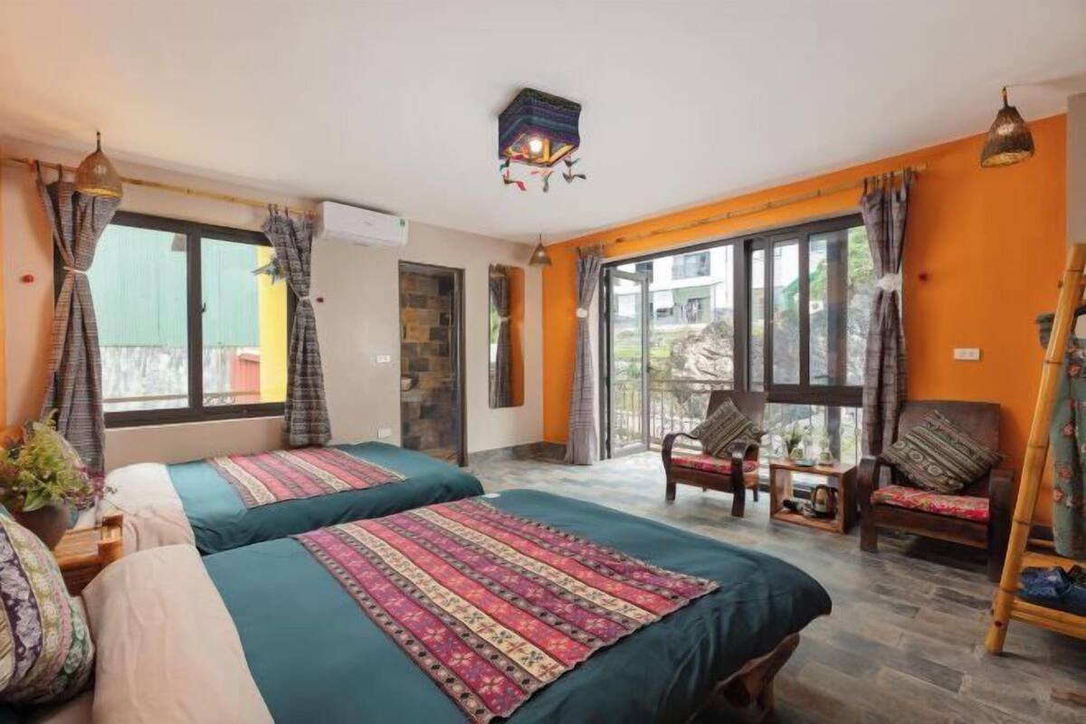 A room with two beds, a sofa, a chair, a small table, and a large window.