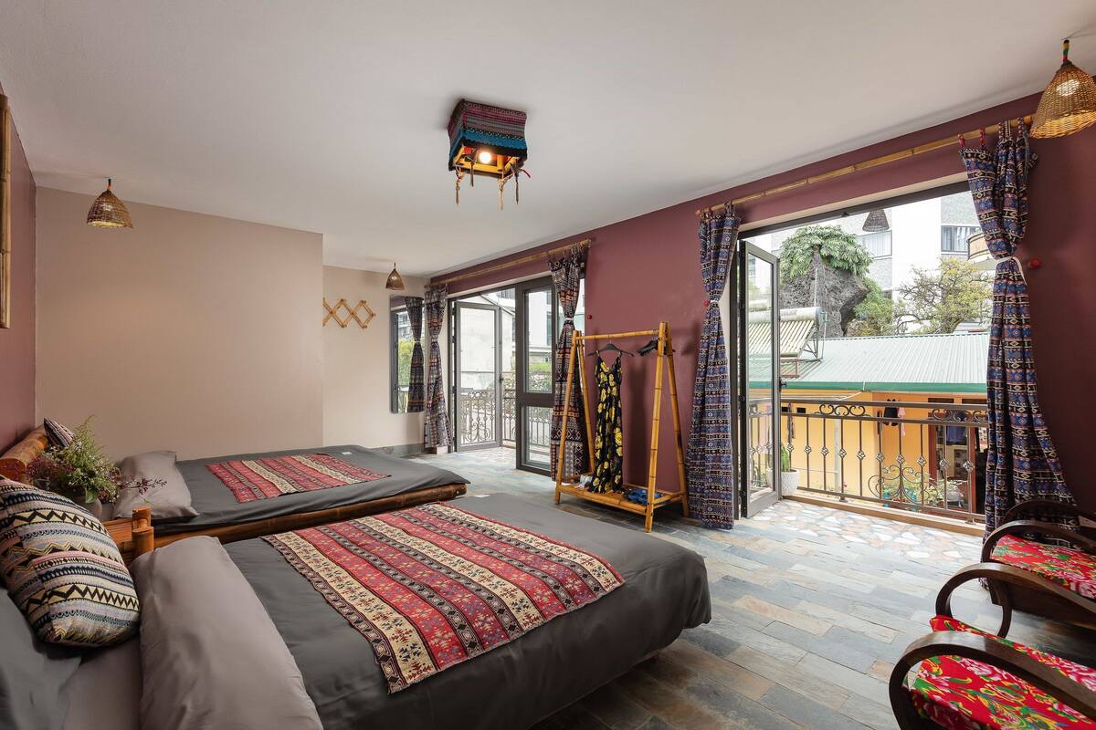A room with two beds, a balcony with a swing, and a view of the outside.