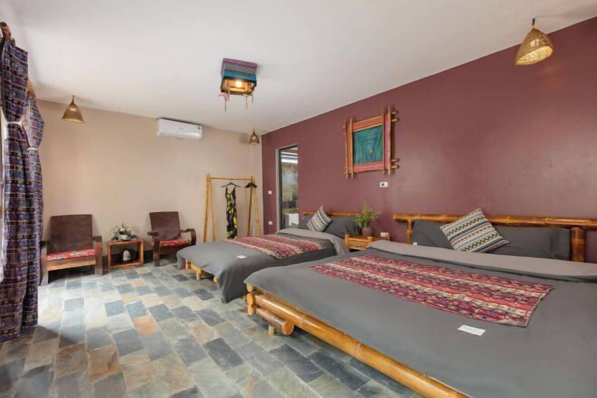 A room with two beds, a wooden headboard, a small table, a chair, and a hanging light fixture.