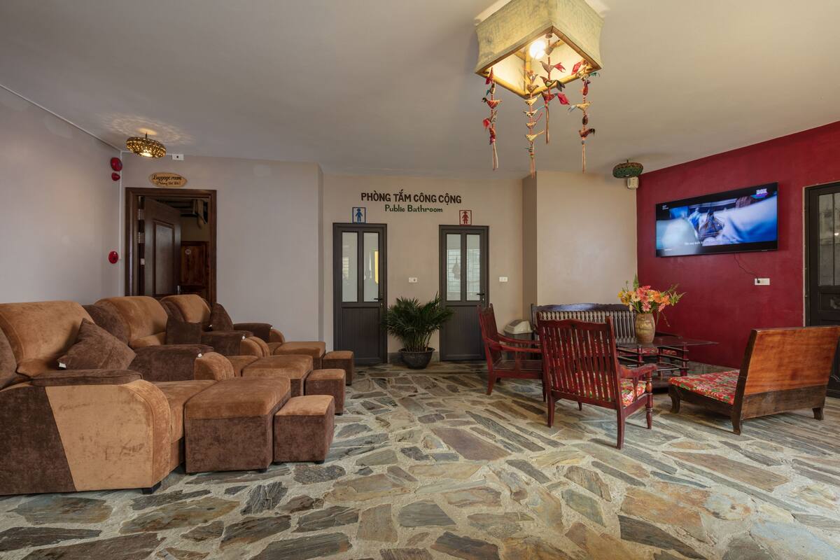 A lobby with a stone floor, sofas, a dining area, and a television screen.