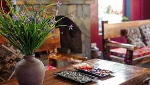Una mesa de madera con un jarrón de flores, un plato de aperitivos y una chimenea de piedra al fondo.