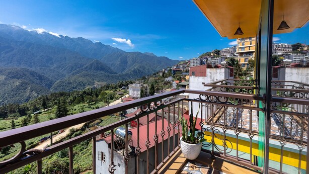 Un balcón con vistas a montañas, un paisaje urbano y una planta en maceta.