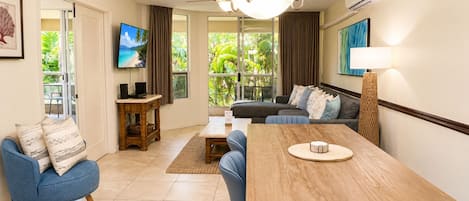Un salon moderne avec un canapé, une table à manger, un téléviseur et une vue sur la verdure à l’extérieur.