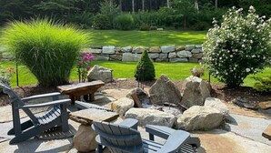 An outdoor seating area with Adirondack chairs and a picnic table, surrounded by large rocks and greenery. - Hidden Oasis in the Mountains by Evergreen Home (Pittsfield)