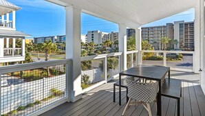 A covered outdoor area with a table and chairs, overlooking a street with buildings and palm trees. - Red Fish Blue Fish🐟Private Pool Home👙Dogs OK🐶 (Okaloosa Island)