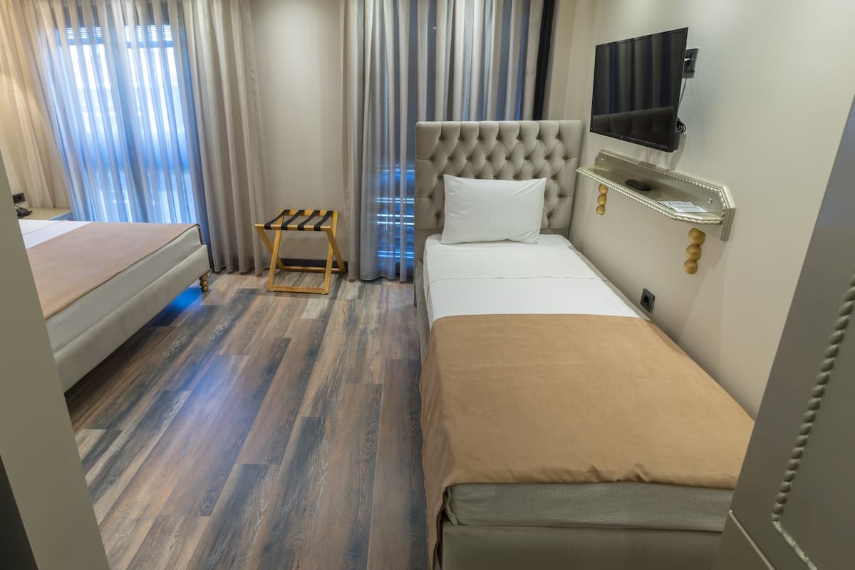 A hotel room with a bed, a small table, a TV, and a window with curtains.
