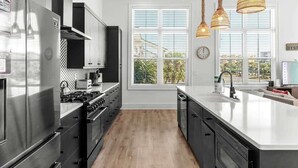 A modern kitchen with stainless steel appliances, a large island, and a view of the outdoors through large windows. - 1 Fish 2 Fish🐟Private Pool Home👙Dogs OK🐶 (Okaloosa Island)