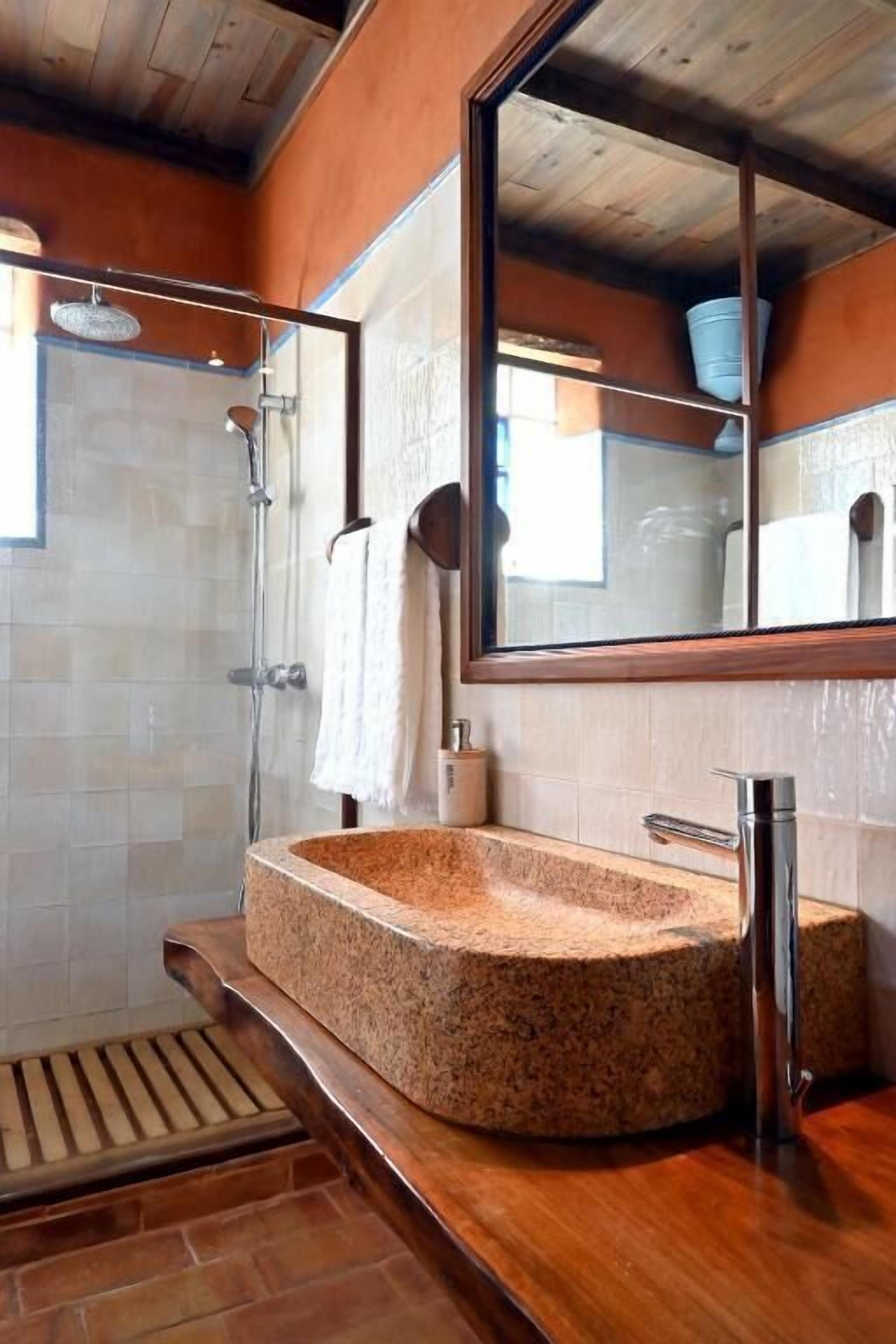 A bathroom with a granite sink, a large mirror, a shower, and a wooden ceiling.