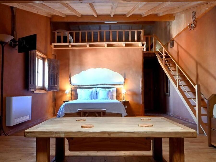 A cozy room with a bed, a wooden table, a bench, and a staircase.