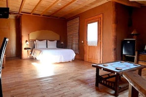Camera da letto con pavimento in legno, un letto, un tavolo e una televisione.