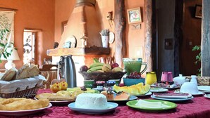 A breakfast buffet with various foods and drinks, a coffee pot, and a rustic interior with wooden beams and a chimney. - Casal da Serra (Penha Garcia)
